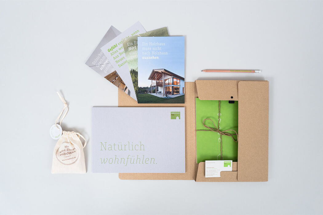 Ein Infopaket über Hausbau aus Holz liegt geöffnet auf einem Tisch, mit Broschüren und einer grünen Mappe.