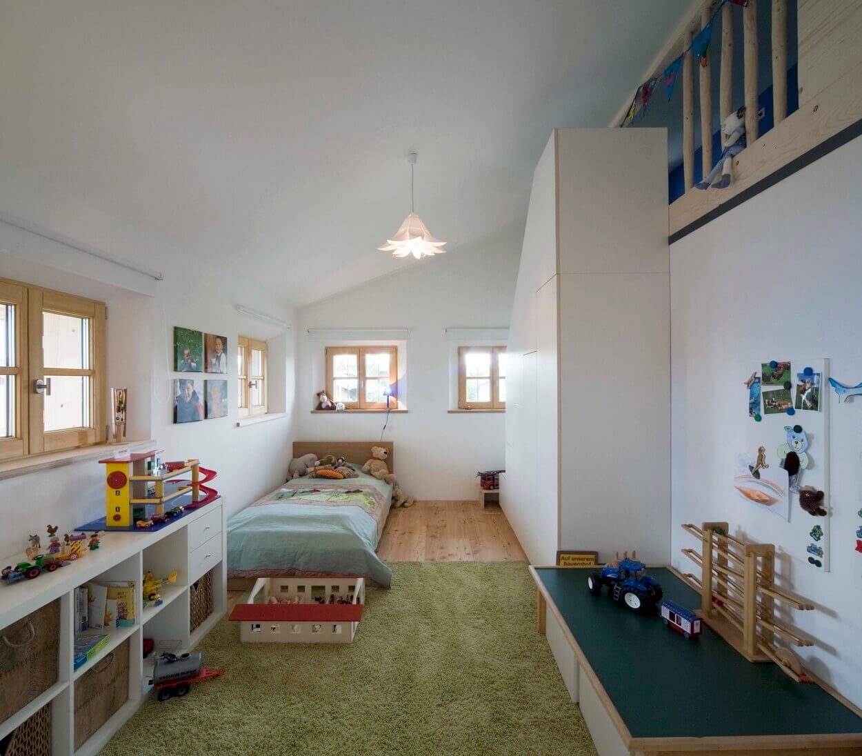 Ein gemütliches Kinderzimmer im Passivhaus-Stil mit Bett, Spielzeug und Spielbereich auf einem grünen Teppich.