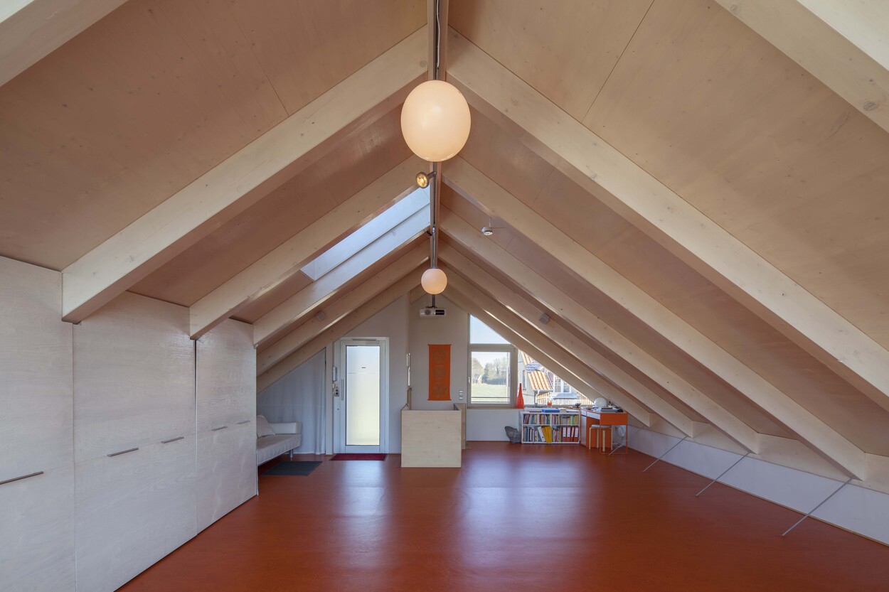 Ein moderner Dachboden in einem Passivhaus in Fürstenfeldbruck mit Holzverkleidung und orangem Boden.