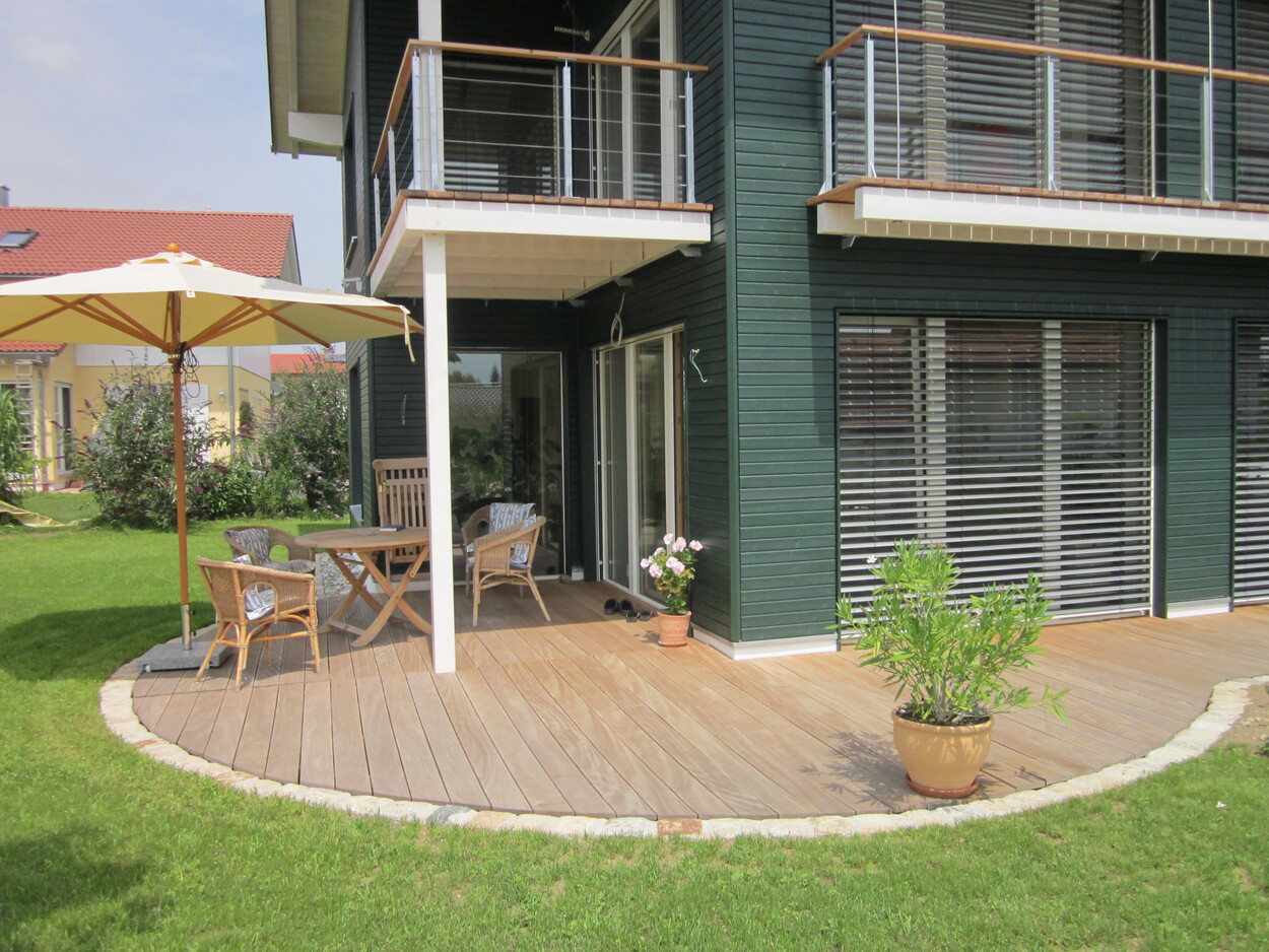 Eine Terrasse eines modernen Passivhauses in Breitbrunn mit Holzmöbeln und Sonnenschirm lädt zum Entspannen ein.