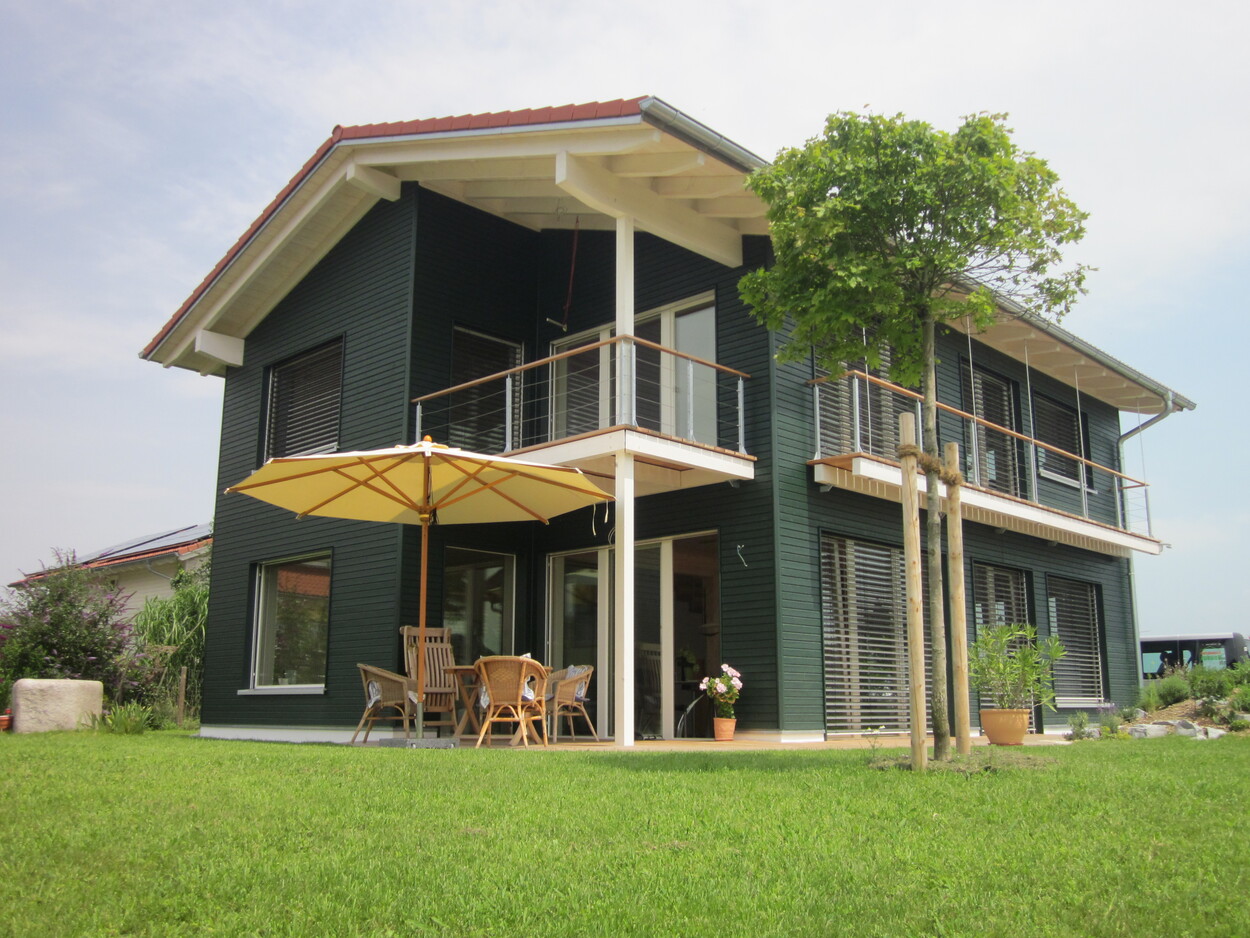 Ein modernes Passivhaus in Breitbrunn mit Holzterrasse und Sonnenschirm, umgeben von einem gepflegten grünen Garten.