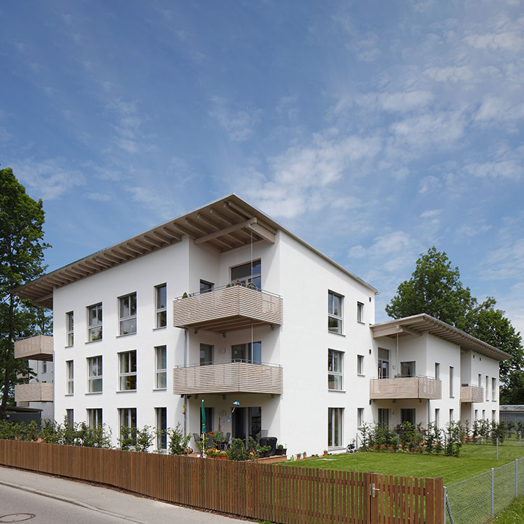 Ein modernes Passivhaus mit weißen Fassaden und Balkonen steht unter klarem, blauem Himmel im Koribianspark Heufeld.