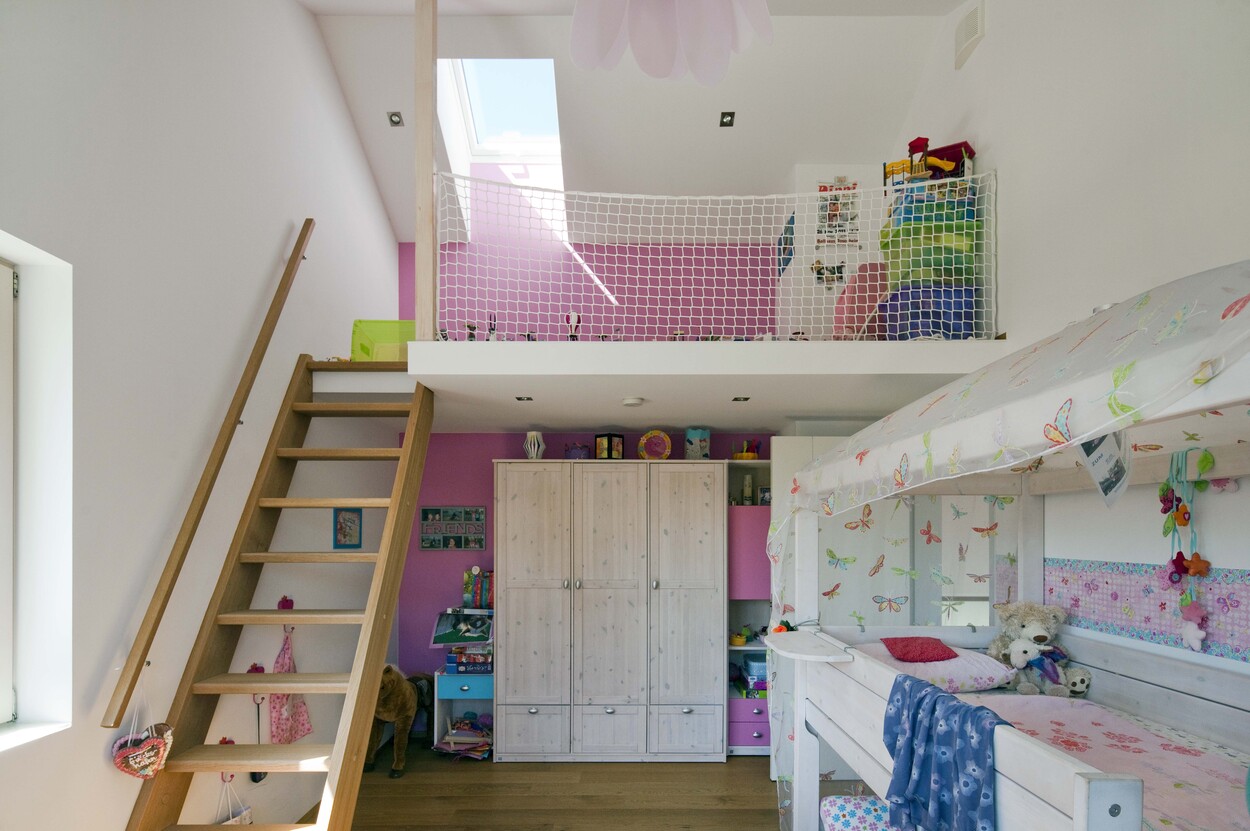 Ein Kinderzimmer in Bad Aibling zeigt ein Hochbett, pinke Wände und Spielzeug auf einem Hochboden im Passivhaus.