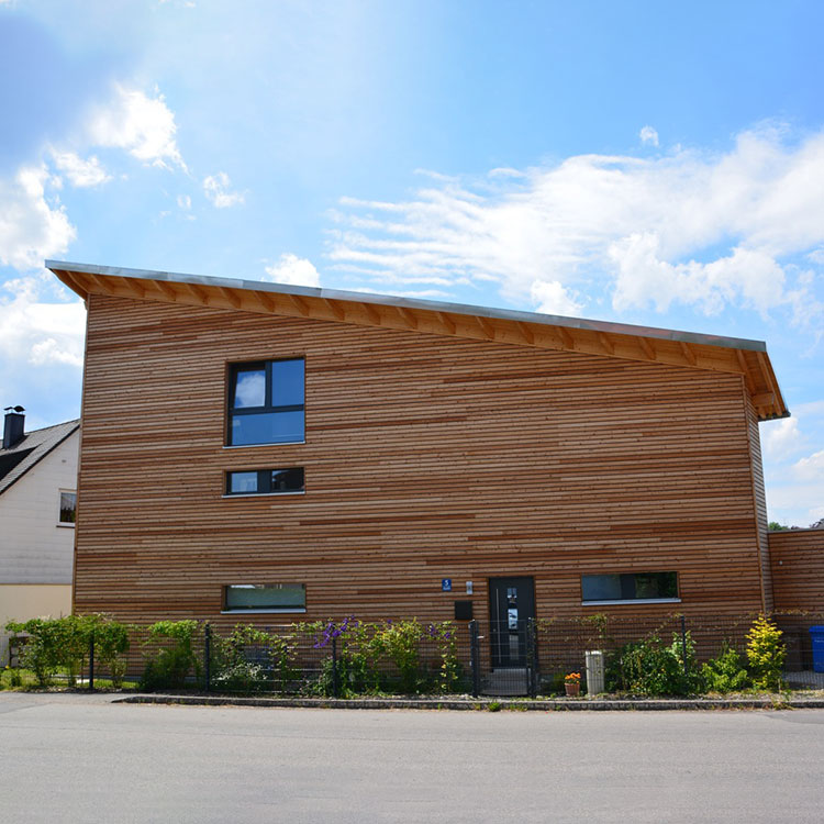 Ein modernes Passivhaus mit Holzfassade steht unter klarem Himmel in München, umgeben von einem kleinen Garten.