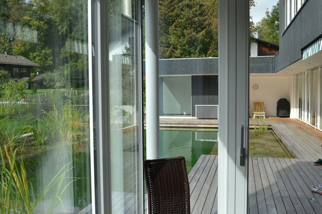 Ein modernes Passivhaus in Brannenburg mit großen Glasfronten eröffnet den Blick auf einen Teich im ruhigen Innenhof.