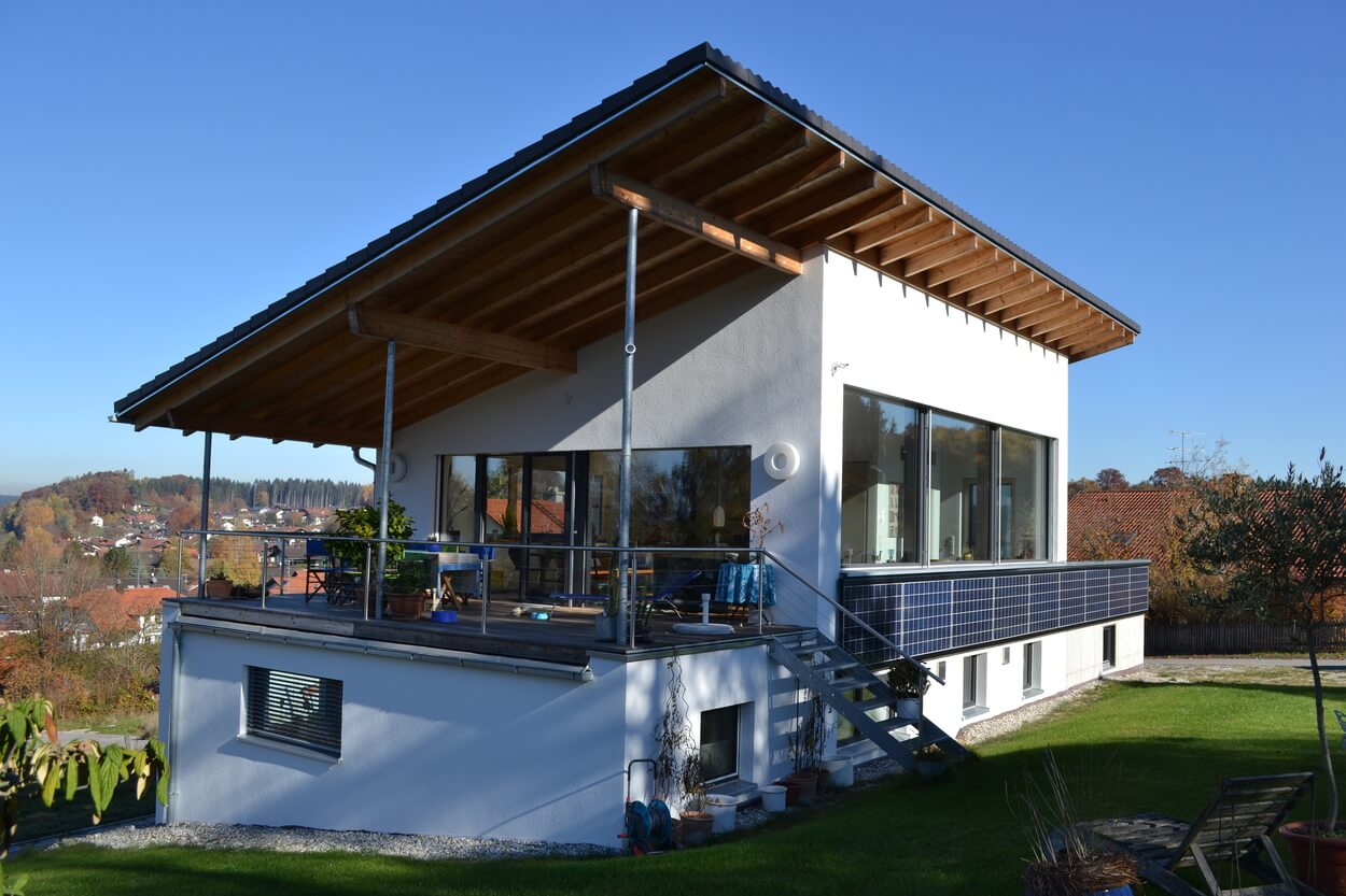 Ein modernes Passivhaus in Soyen mit Solarpanels auf der Terrasse bietet einen weiten Blick auf die Landschaft bei klarem Himmel.