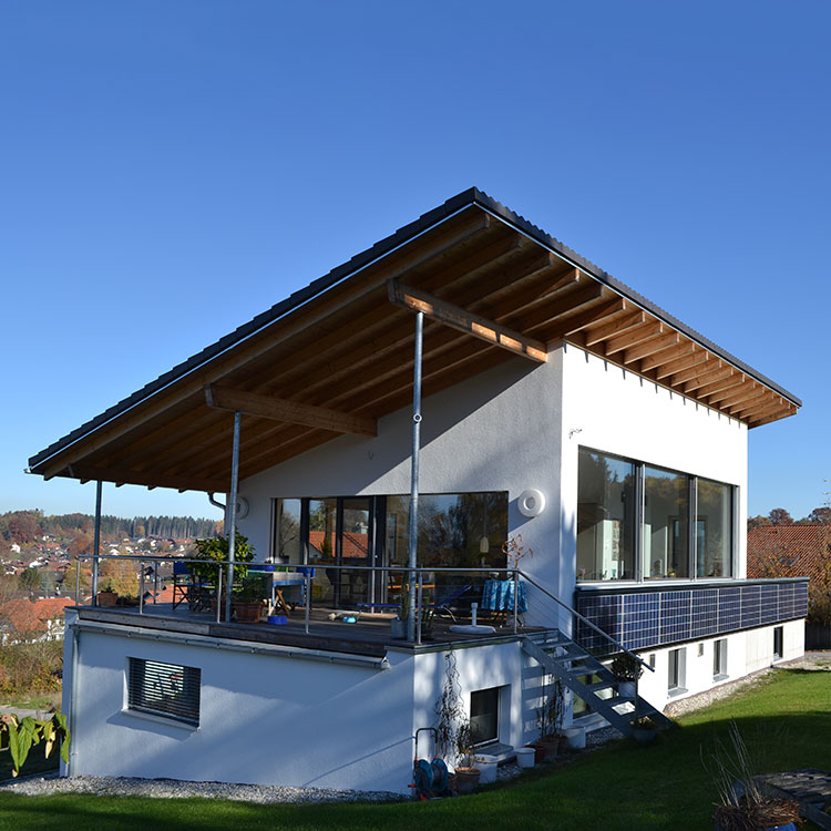 Ein modernes Passivhaus in Soyen mit großen Fenstern und Solarpaneelen auf einer sonnigen Wiese.
