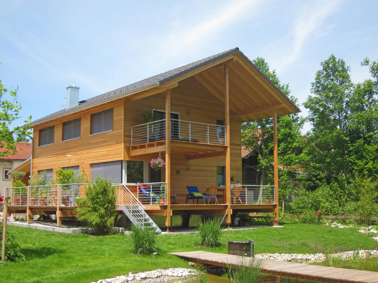 Ein modernes Holzpassivhaus in Glonn steht in einem üppigen Garten mit Teich und großzügiger Terrasse.