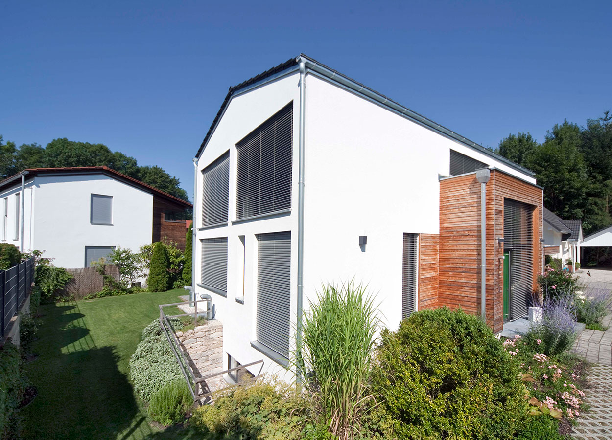 Ein modernes Passivhaus in Ismaning glänzt mit großen Fenstern und gepflegtem Garten unter strahlend blauem Himmel.