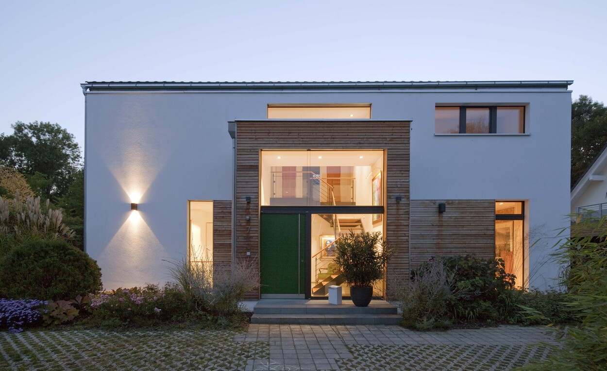 Ein modernes Passivhaus in Ismaning mit Holz- und Glaselementen erstrahlt im warmen Abendlicht.