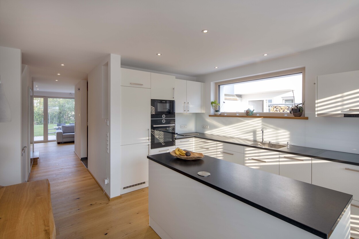 Moderne Küche in einem Doppelhaus in München mit weißen Schränken, großen Fenstern und elegantem Holzboden.