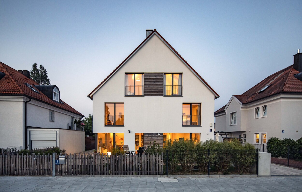 Ein modernes Doppelhaus in München erstrahlt bei Dämmerung mit beleuchteten Fenstern und einem gepflegten Garten.