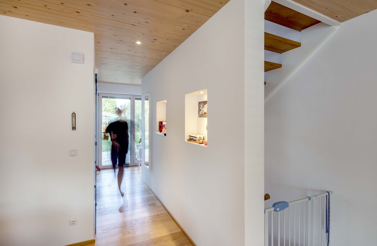 Ein Mann geht durch den modernen Flur eines Doppelhauses in München in Richtung der Terrassentür.