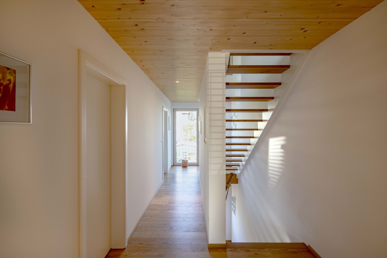 Ein heller Flur mit Holzdecke und Treppe in einem modernen Doppelhaus in München führt zu einem sonnigen Ausgang.