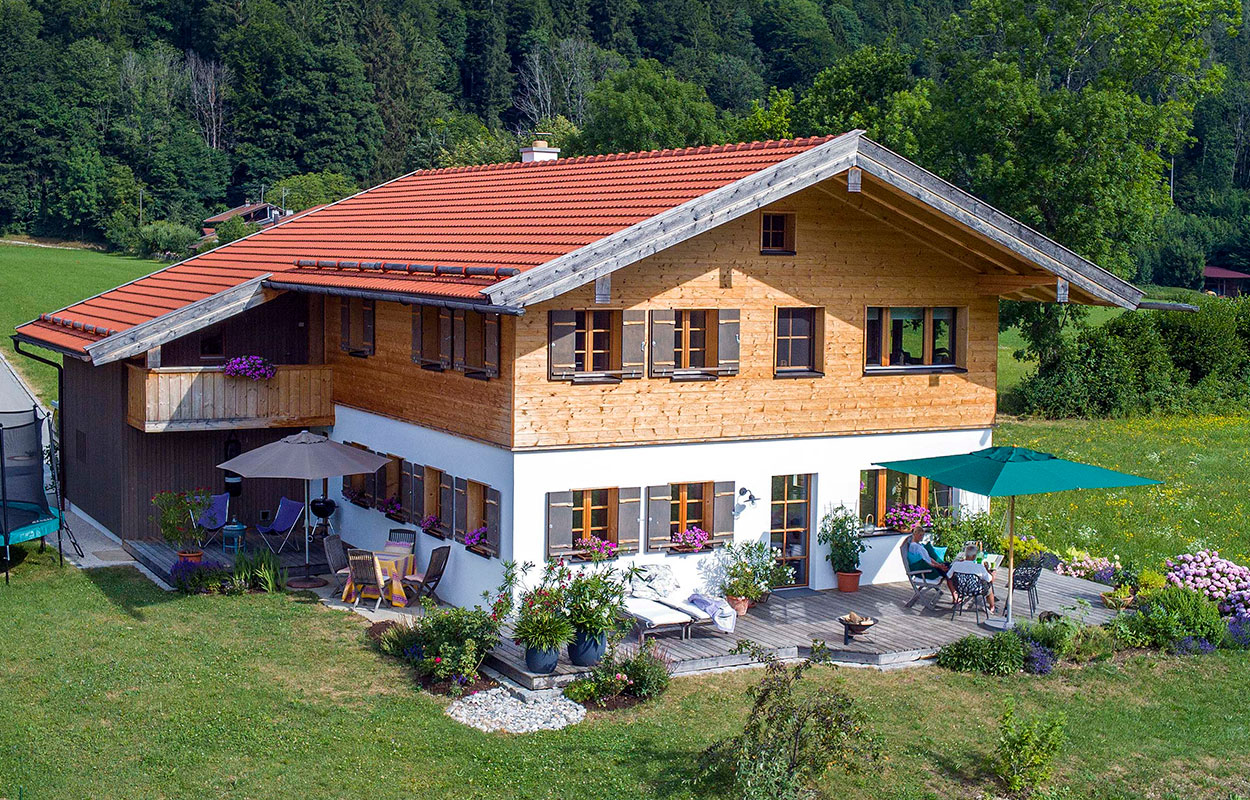 Ein gemütliches Holzhaus in Schleching mit Terrasse, eingebettet in eine grüne Landschaft voller bunter Blumen.
