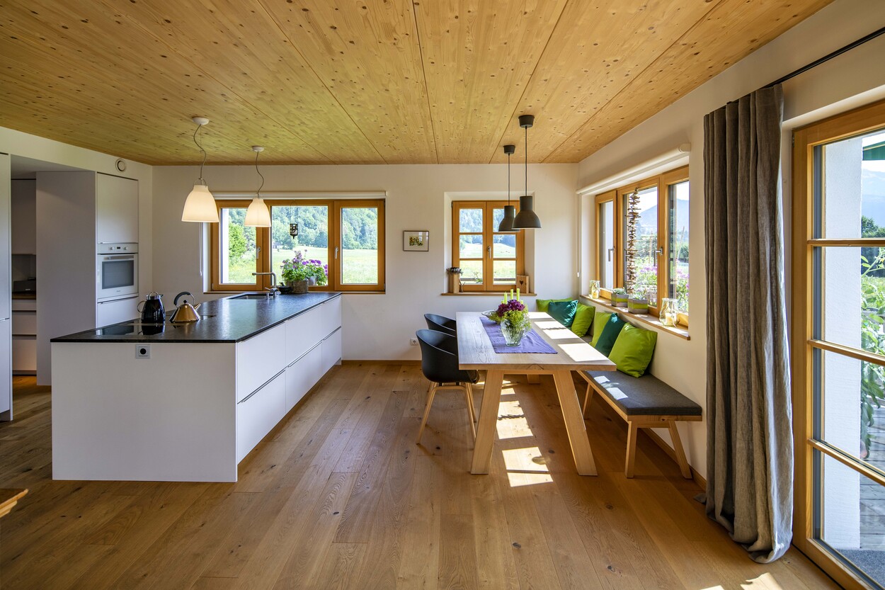 Ein helles Esszimmer in einem Holzhaus in Schleching zeigt moderne Einrichtung und große Fenster mit Blick auf die Natur.