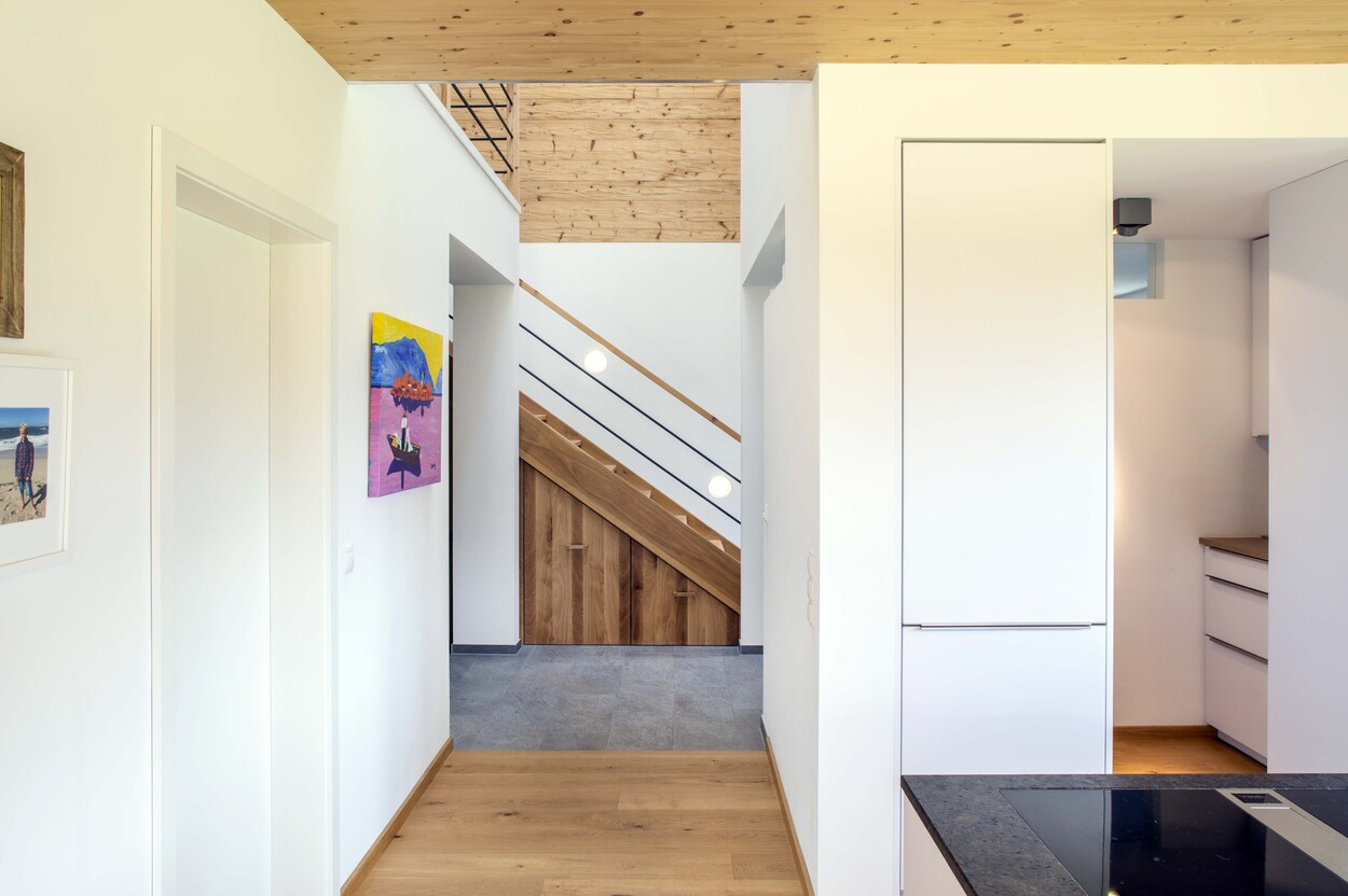 Innenansicht eines modernen Holzhauses in Schleching mit heller Küche, Holztreppe und dekorativen Wandbildern.