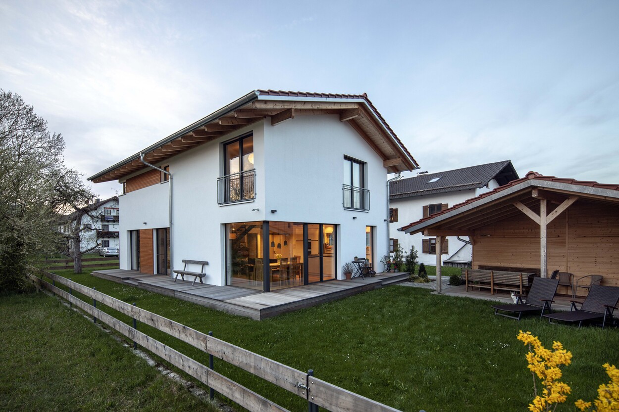 Ein modernes Niedrigenergiehaus in Tuntenhausen mit Holzverkleidung strahlt bei Sonnenuntergang im grünen Garten.