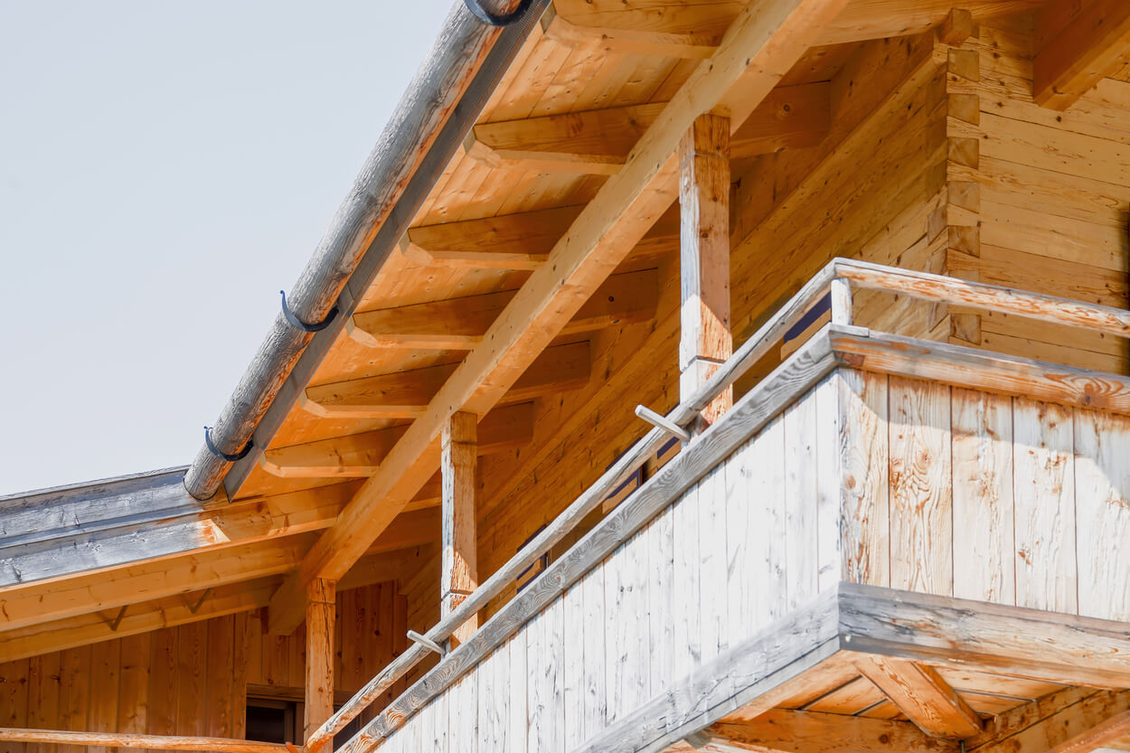Ein hölzerner Balkon und Dach eines Wohnhauses mit Passivhauskomponenten leuchten unter einem strahlend blauen Himmel.