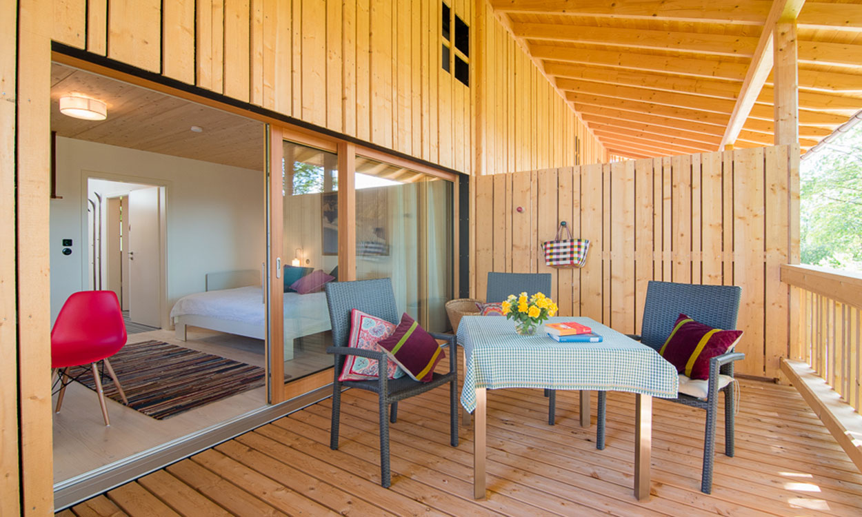 Eine gemütliche Holzterrasse des Passivhauses Wolfsgrube lädt mit Tisch, Stühlen und Blumen zum Entspannen ein.