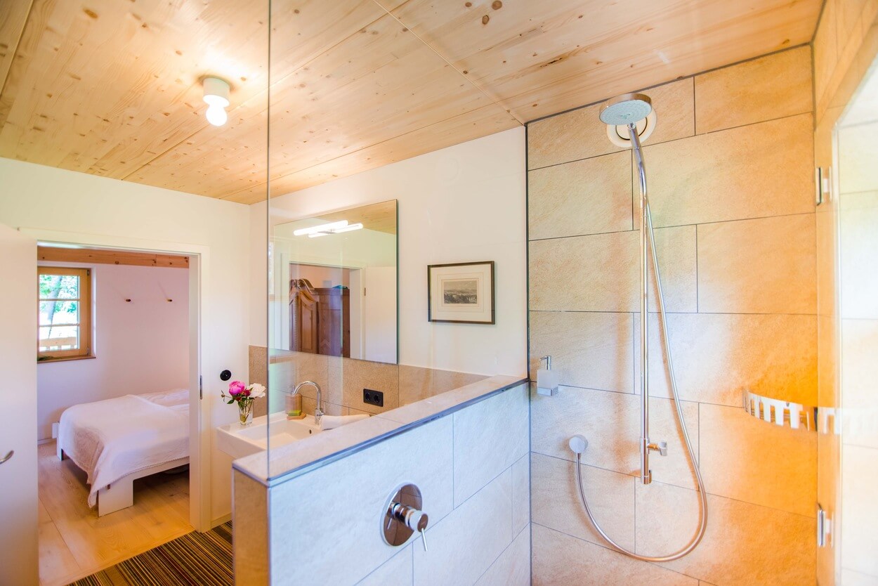Helles Badezimmer im Passivhaus mit moderner Dusche und Blick ins Schlafzimmer mit gemütlichen Holzelementen.