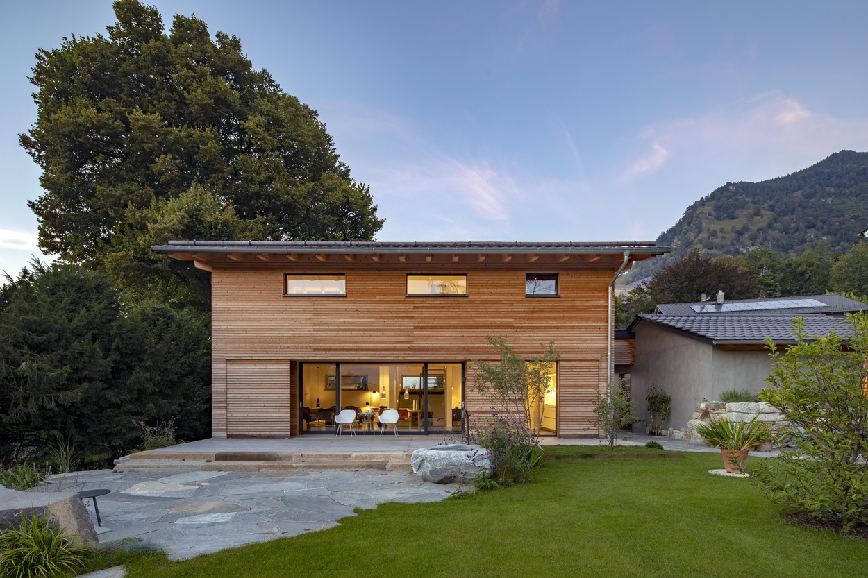 Ein modernes Holzhaus in Marquartstein leuchtet im Abendlicht vor einer beeindruckenden alpinen Kulisse.