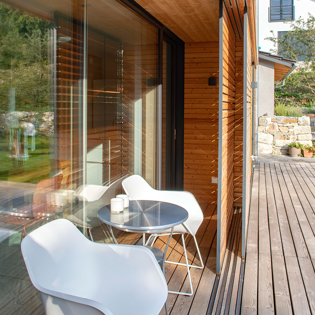 Zwei weiße Stühle und ein Tisch stehen auf der sonnigen Holzterrasse eines modernen Hauses in Marquartstein.