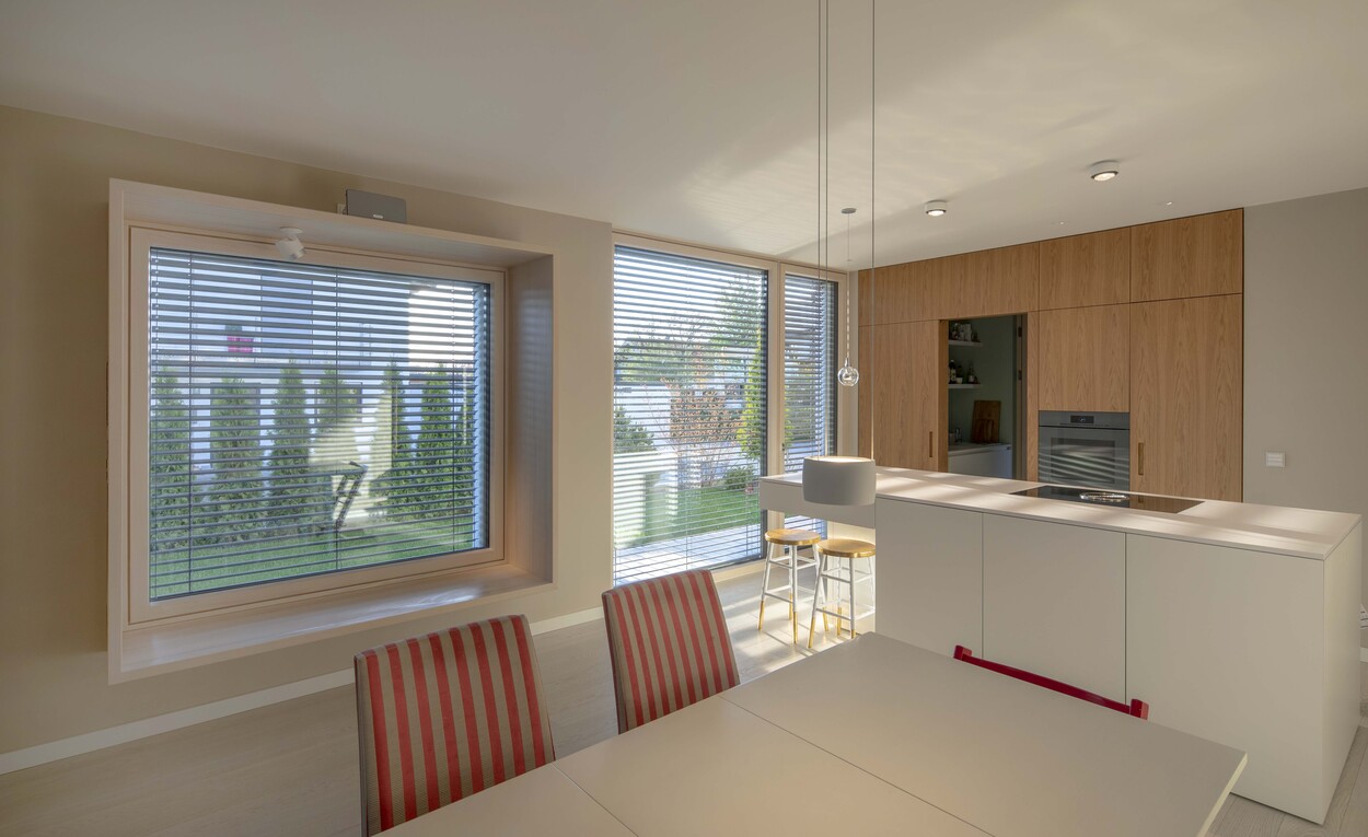 Moderne Küche im Passivhaus Andechs mit Esstisch, großen Fenstern und stilvollen Holzschränken für ein elegantes Ambiente.