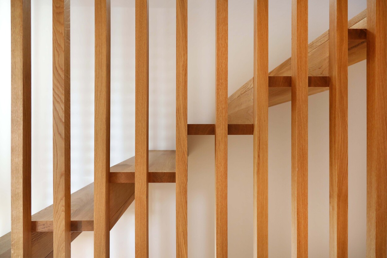 Das Holzgeländer einer modernen Treppe im Passivhaus Andechs betont das minimalistische Design des Raumes.