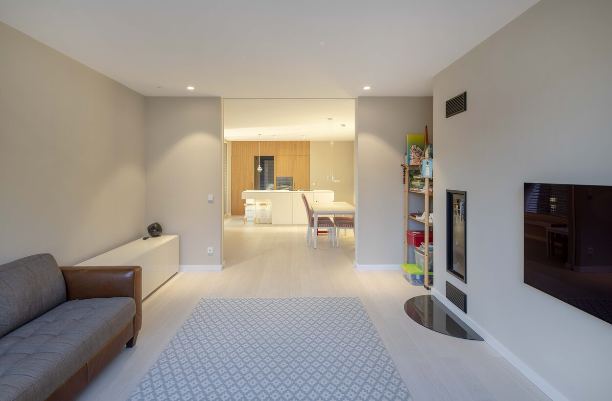 Ein modernes Wohnzimmer im Passivhausstil in Andechs mit gemütlichem Sofa und Blick auf die offene Küche.