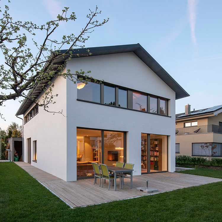 Ein modernes Passivhaus in Andechs mit großen Fenstern und Terrasse, eingebettet in einen gepflegten Garten bei Sonnenuntergang.