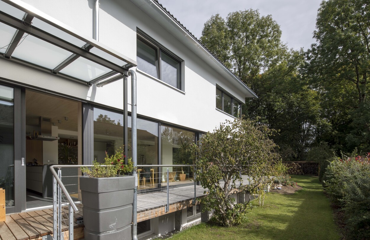 Ein modernes Passivhaus in München mit großer Fensterfront und gepflegtem Garten unter strahlend blauem Himmel.
