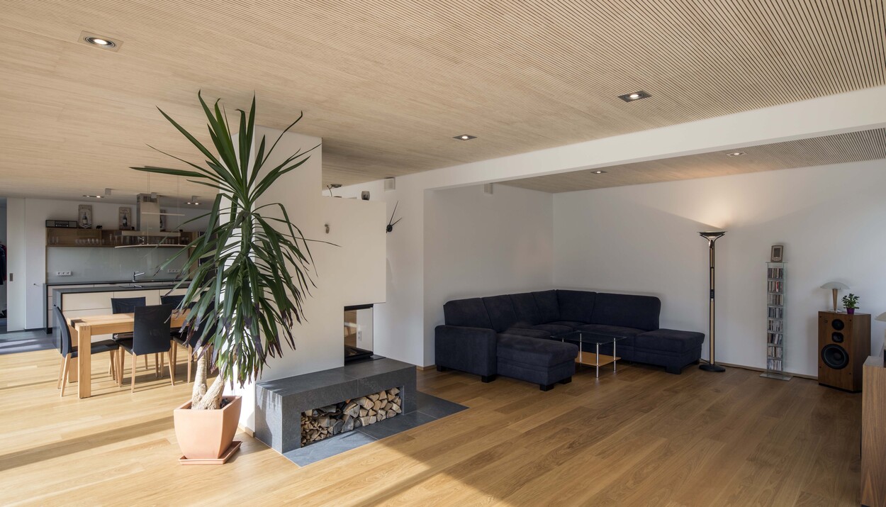 Das Wohnzimmer eines Passivhauses in München bietet eine gemütliche Sitzecke mit Kamin und gestapeltem Holz.