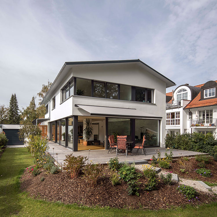 Ein modernes Passivhaus in München steht im Mittelpunkt eines gepflegten Gartens mit Terrasse und gemütlichen Sitzgelegenheiten.