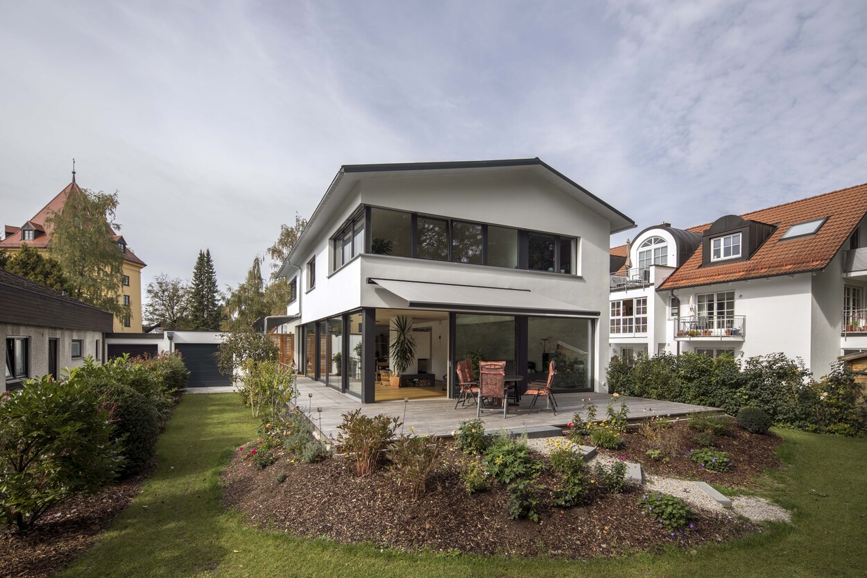 Ein modernes Passivhaus in München mit großen Fensterfronten und gepflegtem Garten unter klarem Himmel.