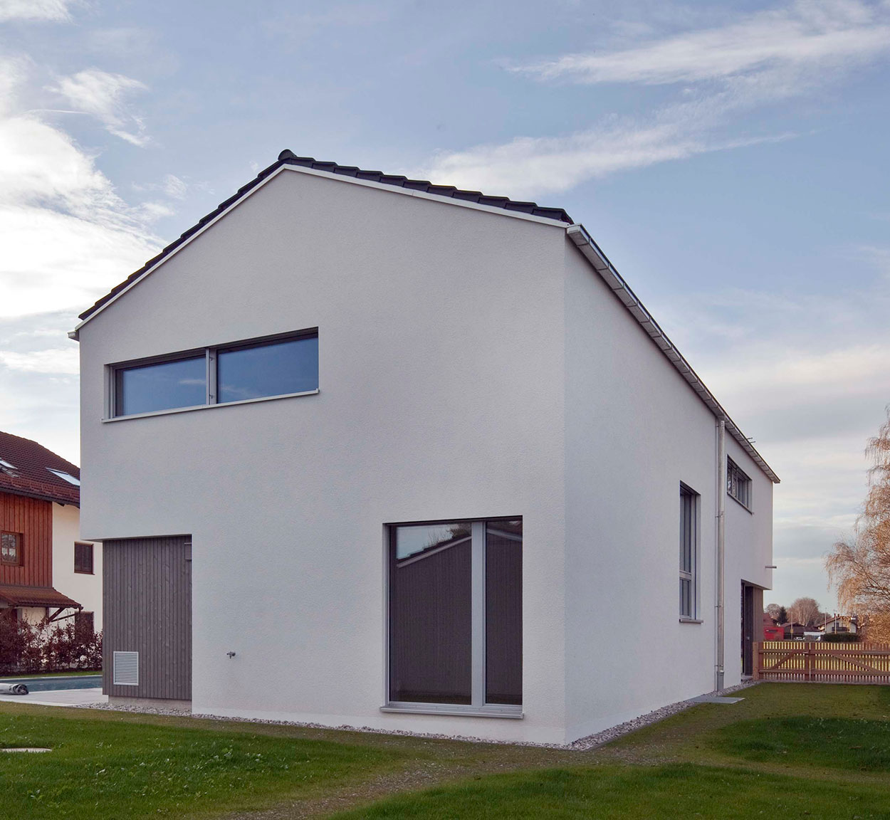 Ein modernes Passivhaus in Bruckmühl steht neben einem gepflegten Rasen unter einem klaren Himmel.