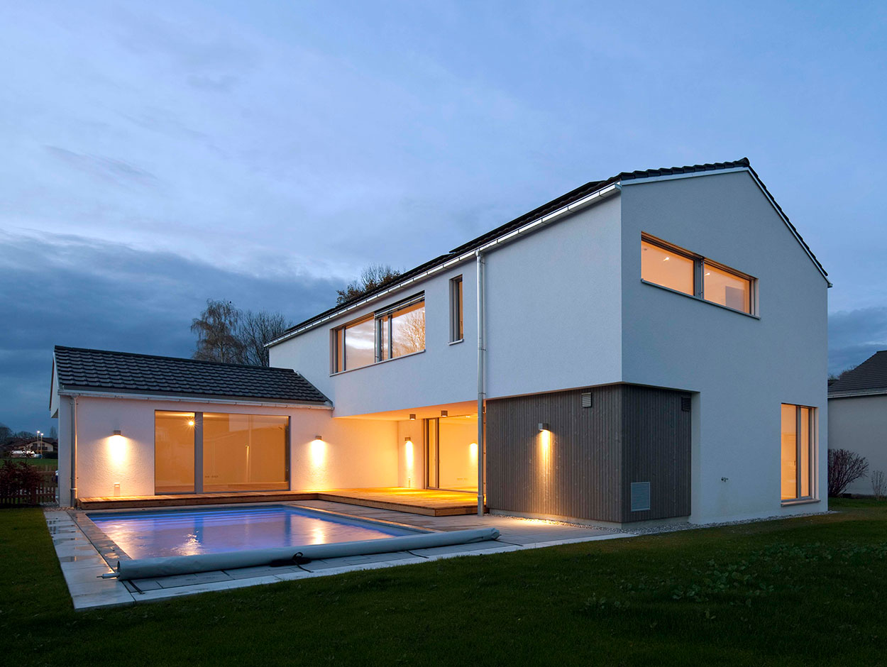 Ein modernes Passivhaus in Bruckmühl mit beleuchtetem Pool erstrahlt bei Abenddämmerung in warmem Licht.