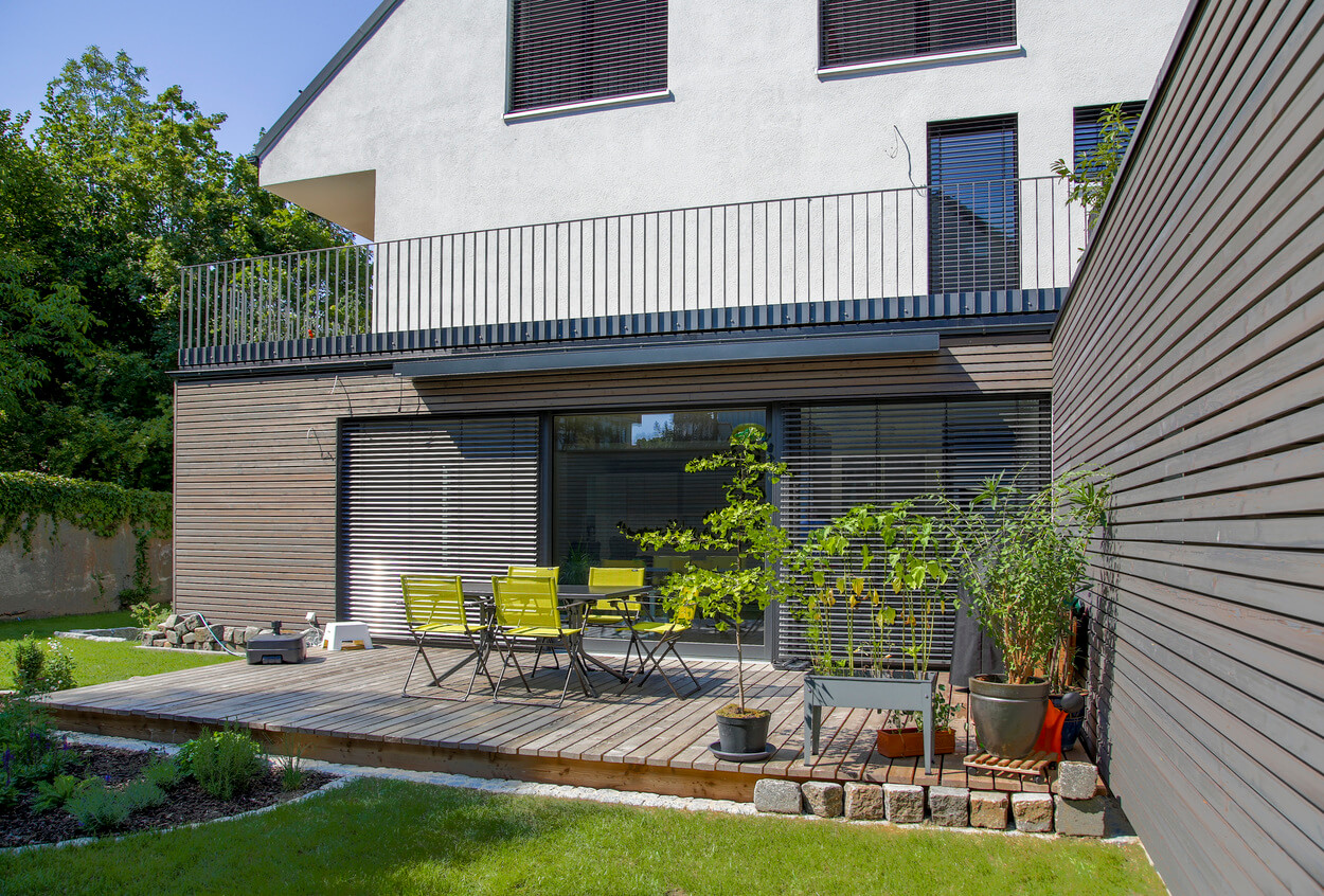 Ein modernes Passivhaus-Doppelhaus in München mit Holzverkleidung und Gartenmöbeln auf der Terrasse im gepflegten Garten.