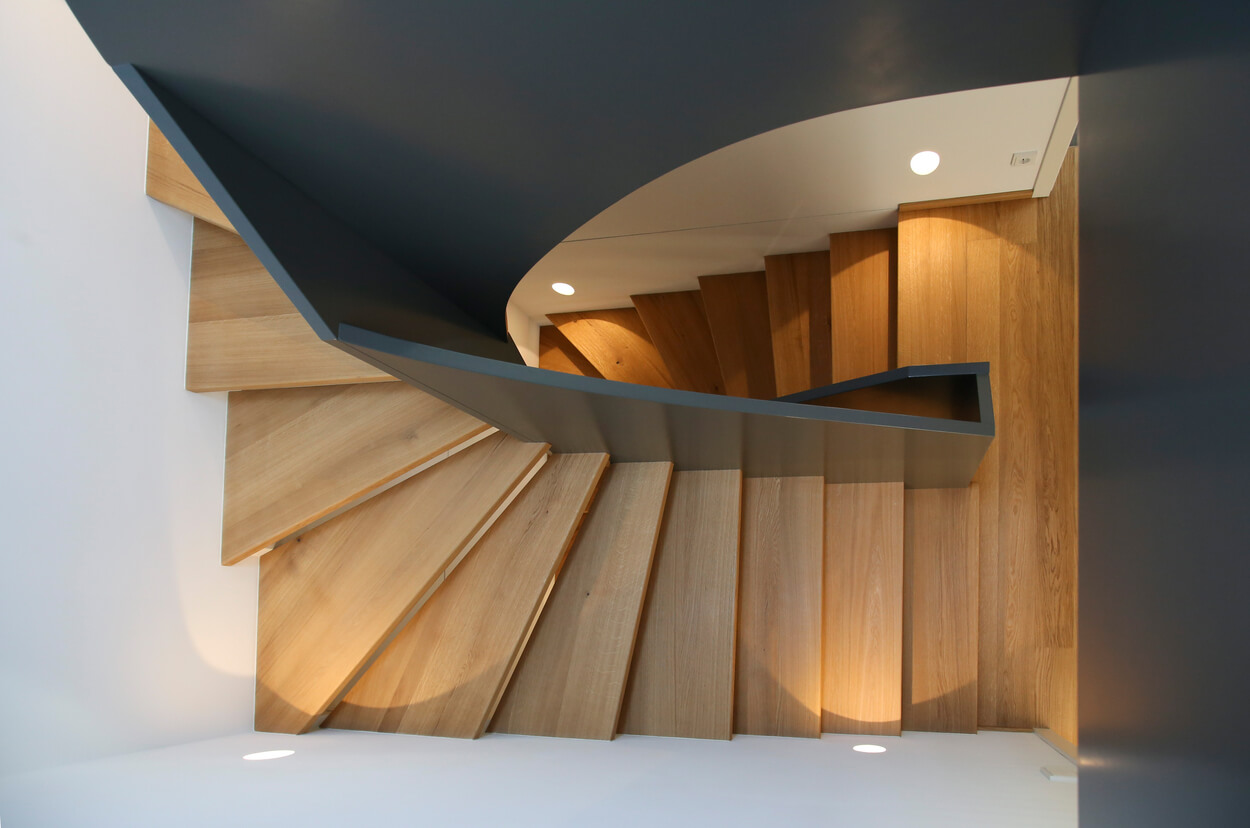 Eine elegante Holztreppe windet sich in einem Münchner Passivhaus spiralförmig nach unten.