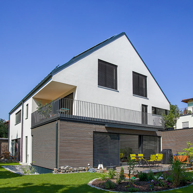 Ein modernes Passivhaus-Doppelhaus in München mit Balkon und gepflegtem Garten unter strahlend blauem Himmel.