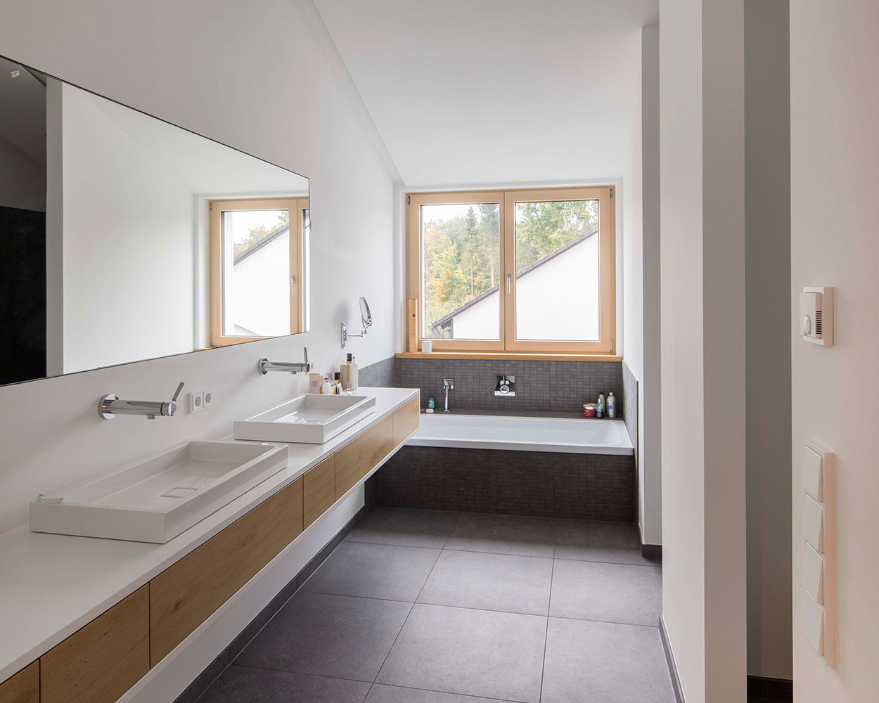 Ein modernes Badezimmer in einem energiesparenden Holzhaus in Putzbrunn mit großen Fenstern und stilvollen Waschbecken.