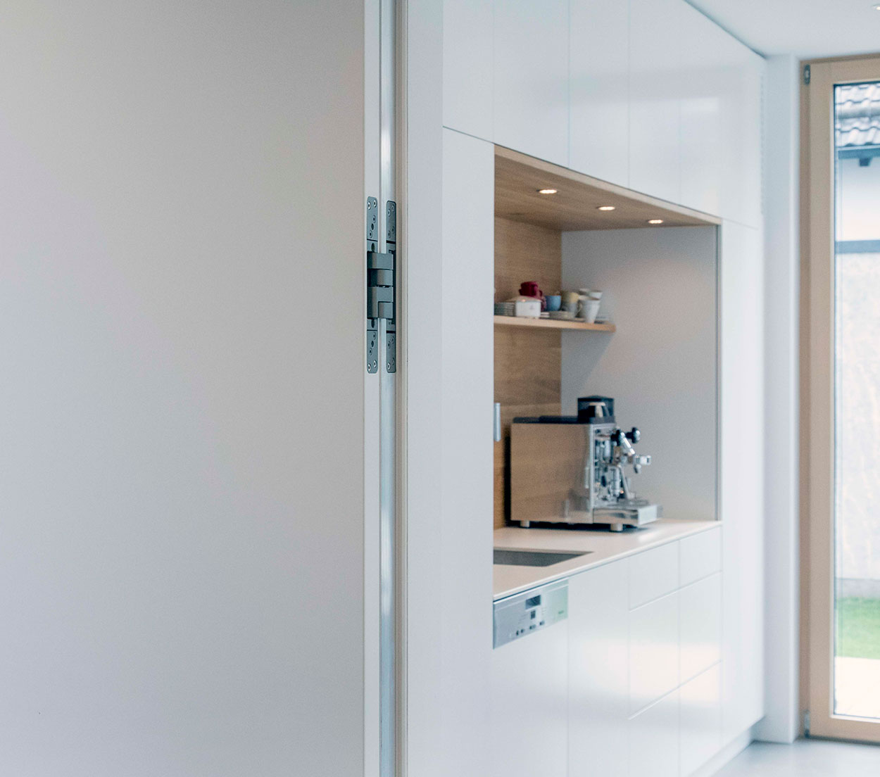 In einer modernen Küche in einem energiesparenden Holzhaus in Putzbrunn steht eine Kaffeemaschine auf weißen Schränken.