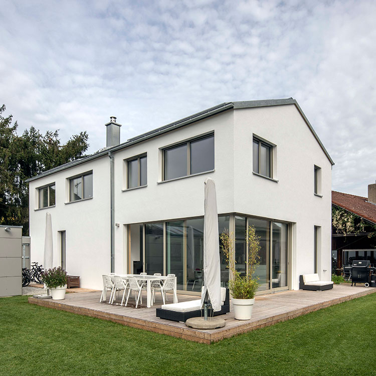 Ein modernes Energiesparhaus aus Holz in Putzbrunn mit Terrasse und Garten unter einem bewölkten Himmel.