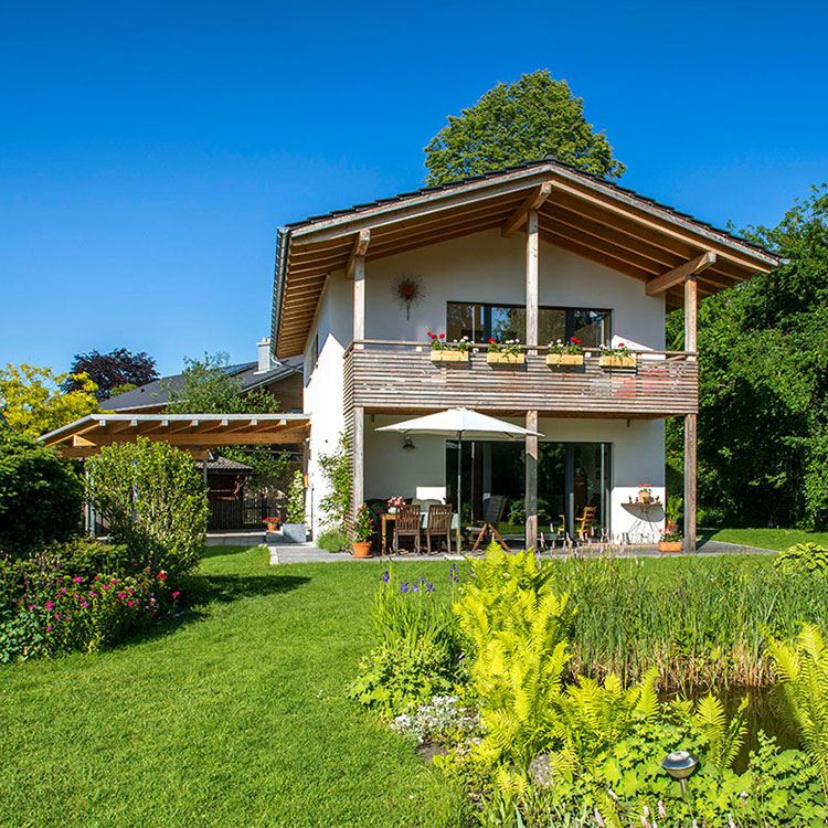 Ein modernes Passivhaus in Bad Aibling steht in einem grünen Garten mit Terrasse und Sonnenschirm.