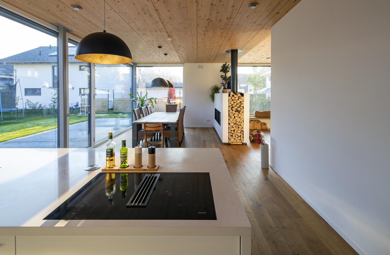 Die moderne Küche in einem Holzhaus in Oberpframmern zeigt große Fenster und einen stilvollen Essbereich mit Holztisch.