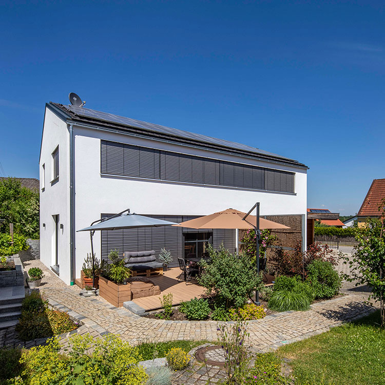 Ein modernes Passivhaus in Fahrenzhausen mit Solarpanelen und gemütlicher Terrasse strahlt bei sonnigem Wetter.