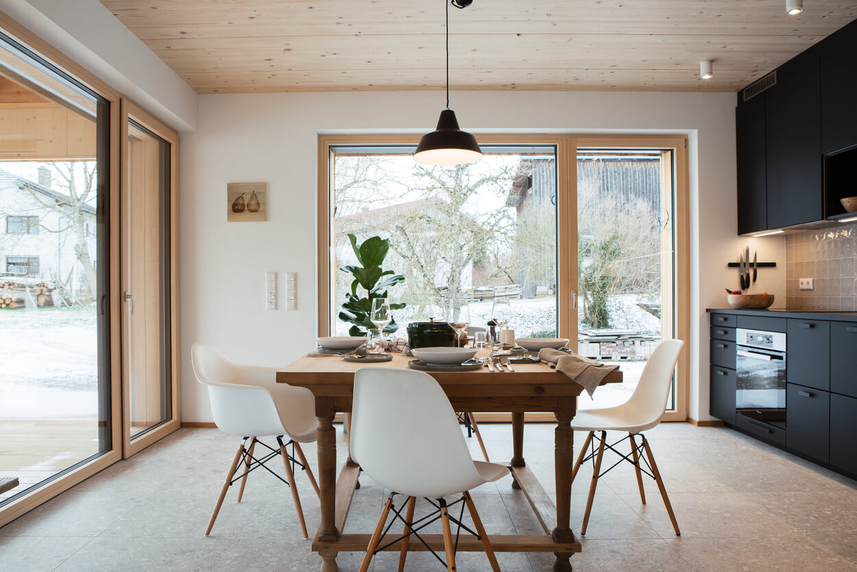 Ein stilvoller Essbereich in einem Holzhaus im Chiemgau mit großen Fenstern und einem elegant gedeckten Tisch.