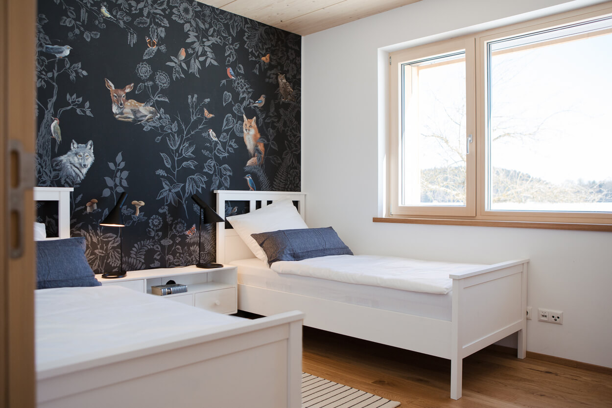 Zwei Einzelbetten stehen in einem hellen Schlafzimmer mit kunstvoller Tier-Tapete in einem Holzhaus im Chiemgau.