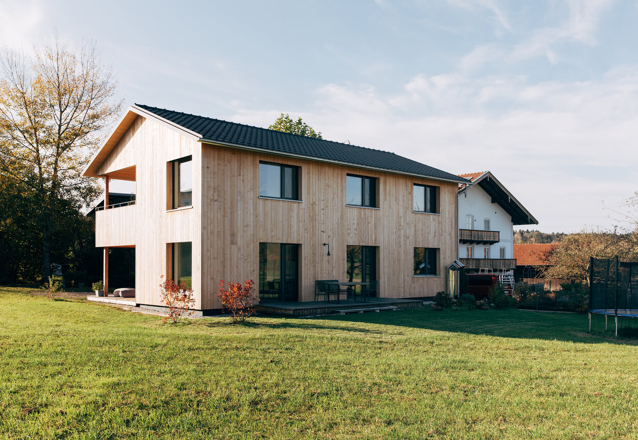 Ein modernes Holzferienhaus im Chiemgau steht auf einer grünen Wiese unter klarem Himmel.