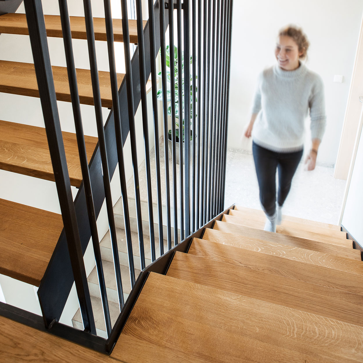 Eine Frau steigt lächelnd die stilvolle Holztreppe in einem modernen Ferienhaus im Chiemgau hinauf.